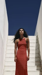 Model Tamar David in a red halter knit maxi dress stands on white outdoor stairs against a deep blue sky for Missoni.