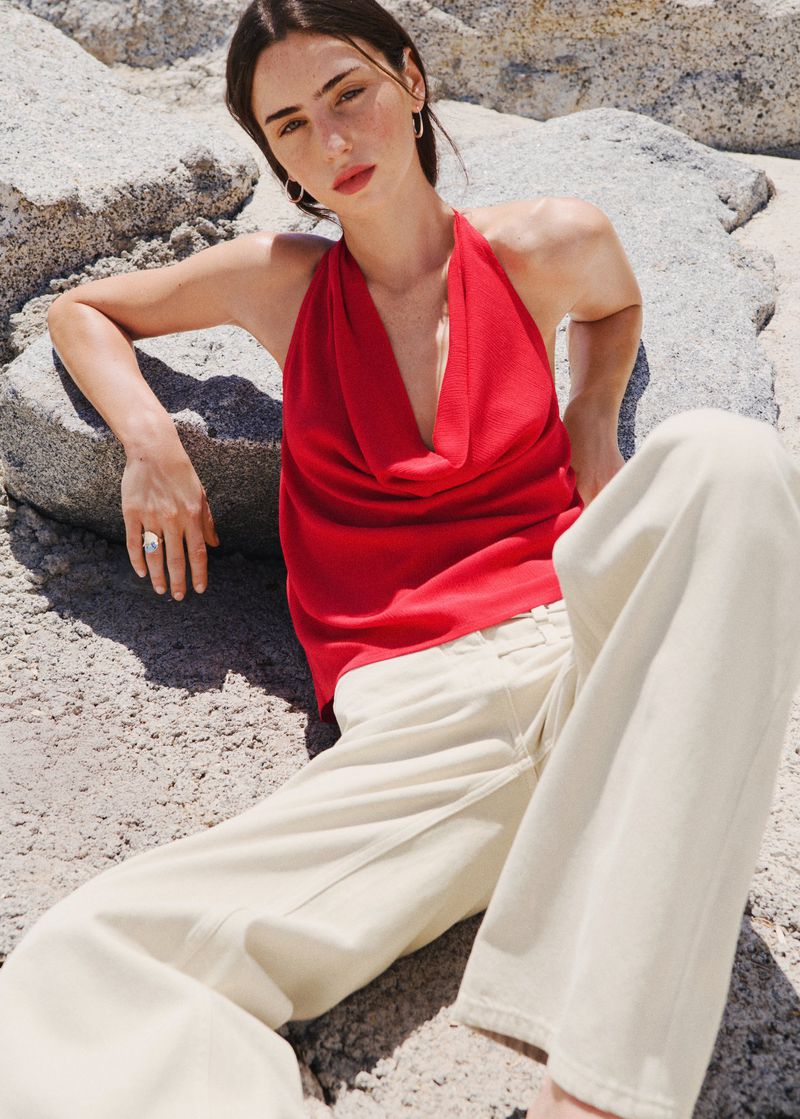 Woman in red halter top and wide white trousers seated against large rock boulders outdoors