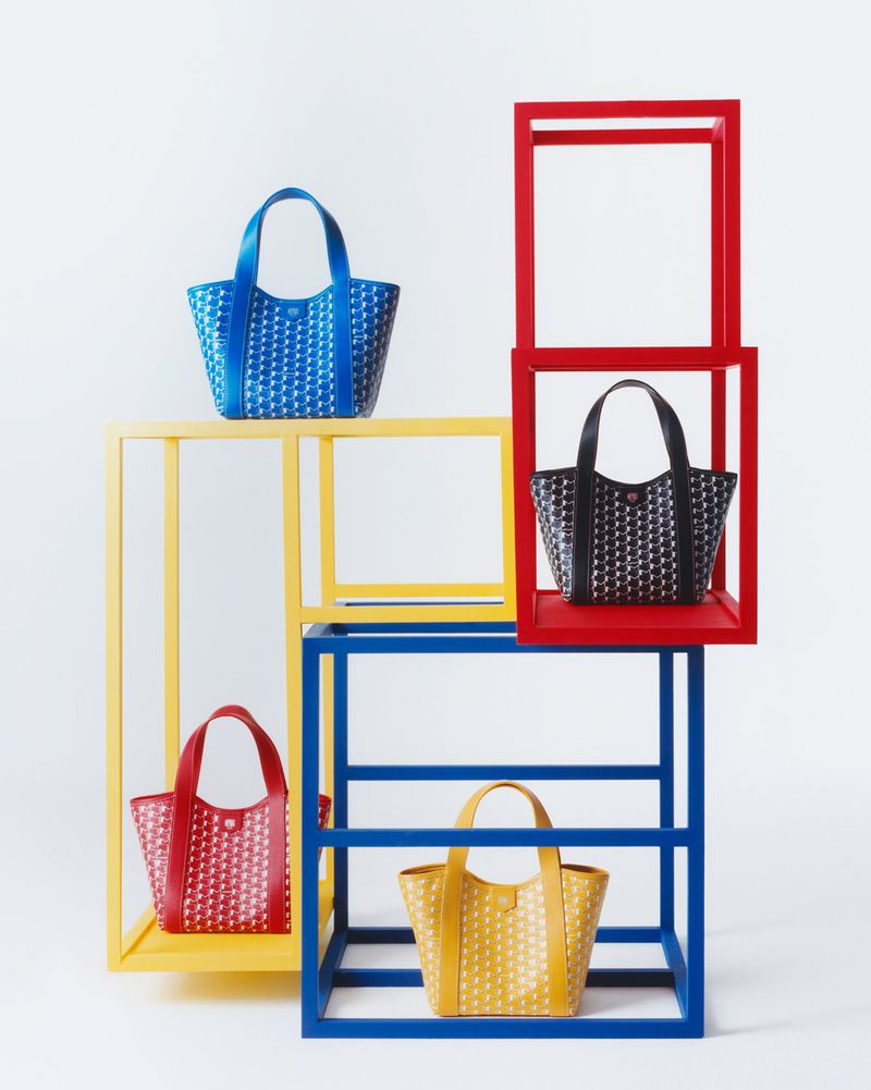 Four patterned tote bags in blue, red, yellow, and black are displayed on blue, red, and yellow geometric shelving against a white backdrop.
