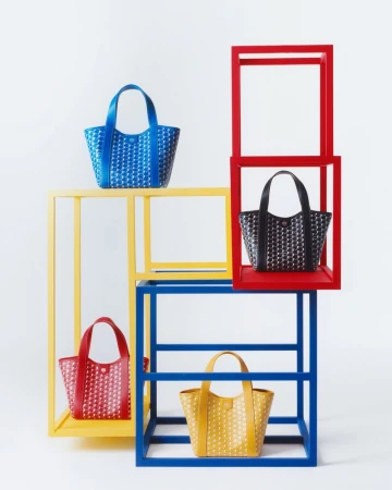 Four patterned tote bags in blue, red, yellow, and black are displayed on blue, red, and yellow geometric shelving against a white backdrop.