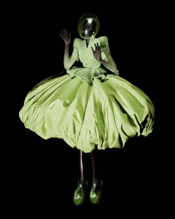 A Black model wearing a sculptural lime green puff dress and clear dome helmet floating against a black seamless backdrop.