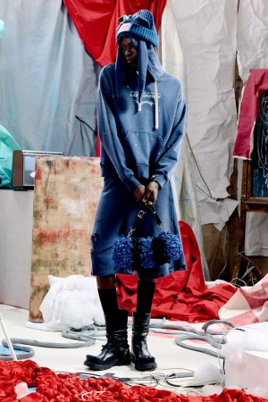 Model Quadri Ajao standing in a blue graphic hoodie, matching shorts, knit ear beanie, and black chunky boots on a styled studio set.