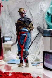 Model Quadri Ajao poses in an avant-garde layered nautical look in a studio set surrounded by vintage television sets.