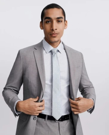 Man in a tailored light grey suit, patterned dress shirt, and light tie posing against a white studio background.