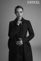 Model Daria Chernenko posing in a structured black jacquard coat and decorative headband against a grey studio backdrop.