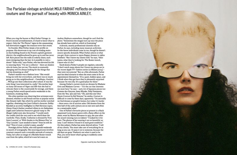 A woman with curly hair wears a paper mask shaped like a person's face in a surreal studio fashion portrait with a neutral background.