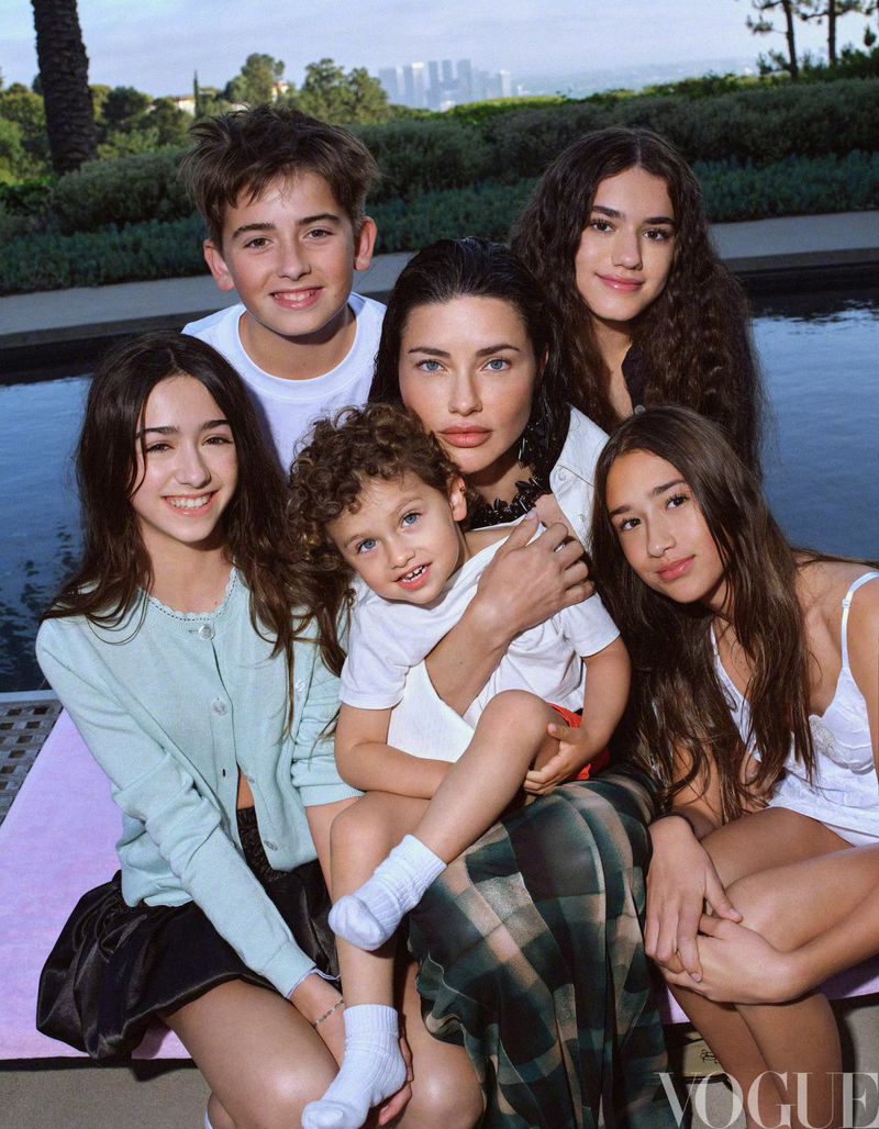 Family portrait featuring a woman with five children of varying ages, photographed outdoors near a pool and cityscape backdrop, Vogue logo visible.