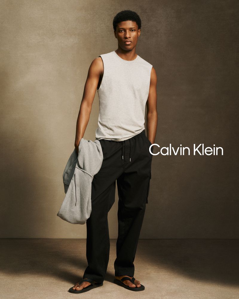 Model Aboubakar Konte wearing a light sleeveless top and black cargo pants against a textured neutral backdrop for Calvin Klein.