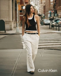 Model walking down a city street wearing a layered black tank top and white wide-leg cargo pants for Calvin Klein.
