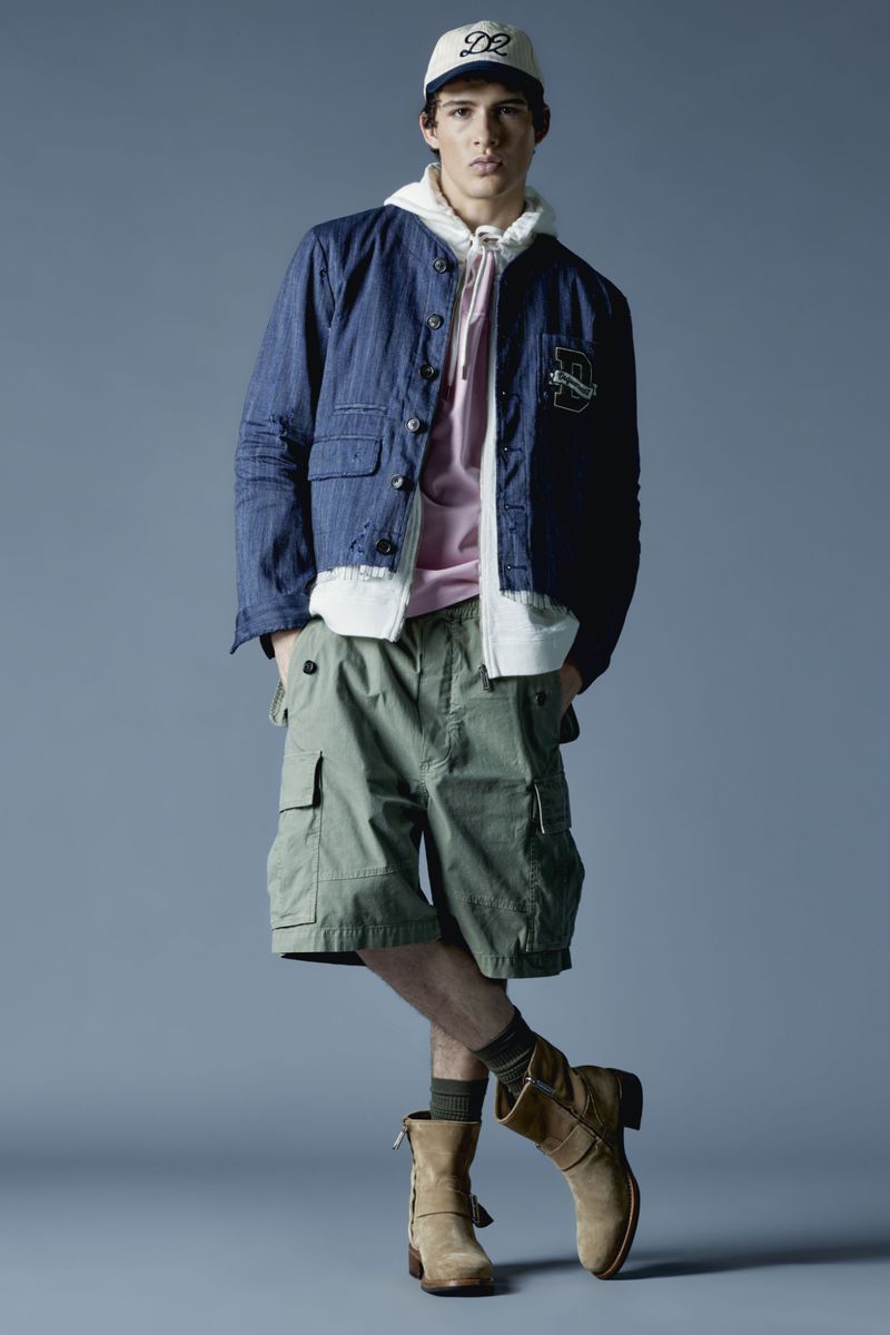 Full-length studio portrait of a young adult male in a hooded sweatshirt, denim jacket, cargo shorts, boots, and a baseball cap.