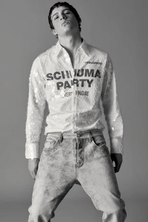 Male model wearing a graphic sequined button-up shirt and textured light-wash denim jeans against a neutral studio backdrop.
