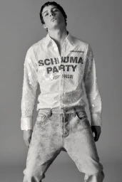 Male model wearing a graphic sequined button-up shirt and textured light-wash denim jeans against a neutral studio backdrop.