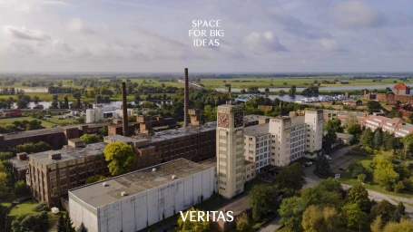 Aerial view of the Veritas historic factory complex featuring a tall clock tower, brick industrial buildings, and surrounding landscape.