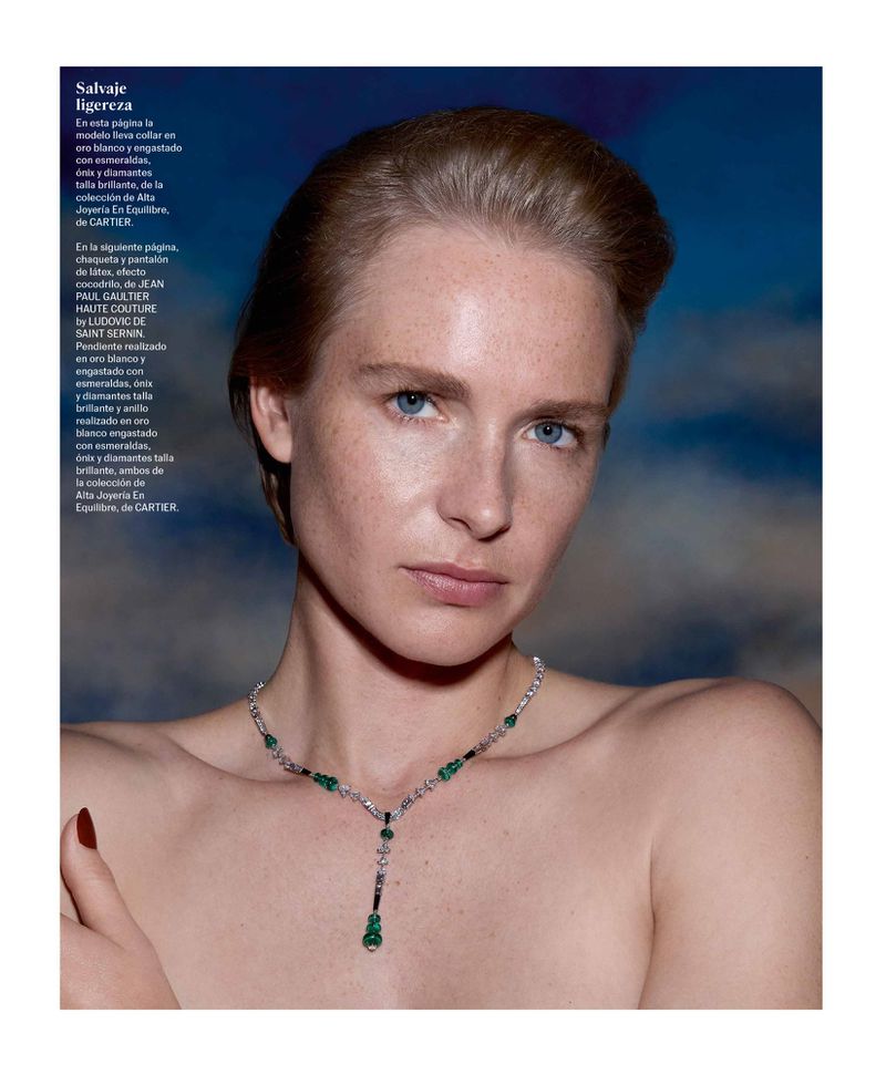Adult woman poses wearing an emerald and diamond necklace against a blue and white background in a beauty and fashion editorial.