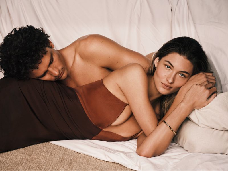 Grace Elizabeth and Simon Nessman reclining together on white bedsheets for the Calvin Klein Refined Campaign 2026.