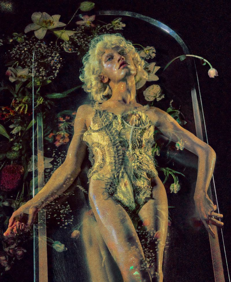 Model with blonde curly hair wearing a textured bodysuit lying among flowers behind glass for Google Pixel Creator Labs by Elizaveta Porodina.