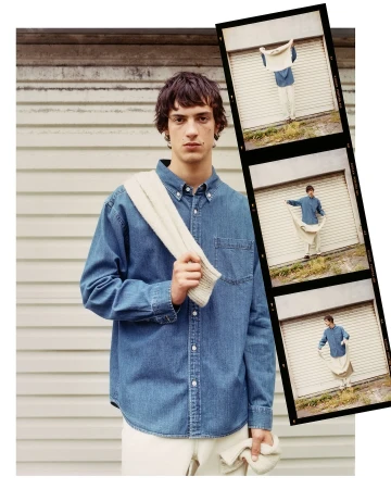 Portrait of a young adult man in a denim shirt with a sweater over his shoulder posing in front of a garage door with film strip images.