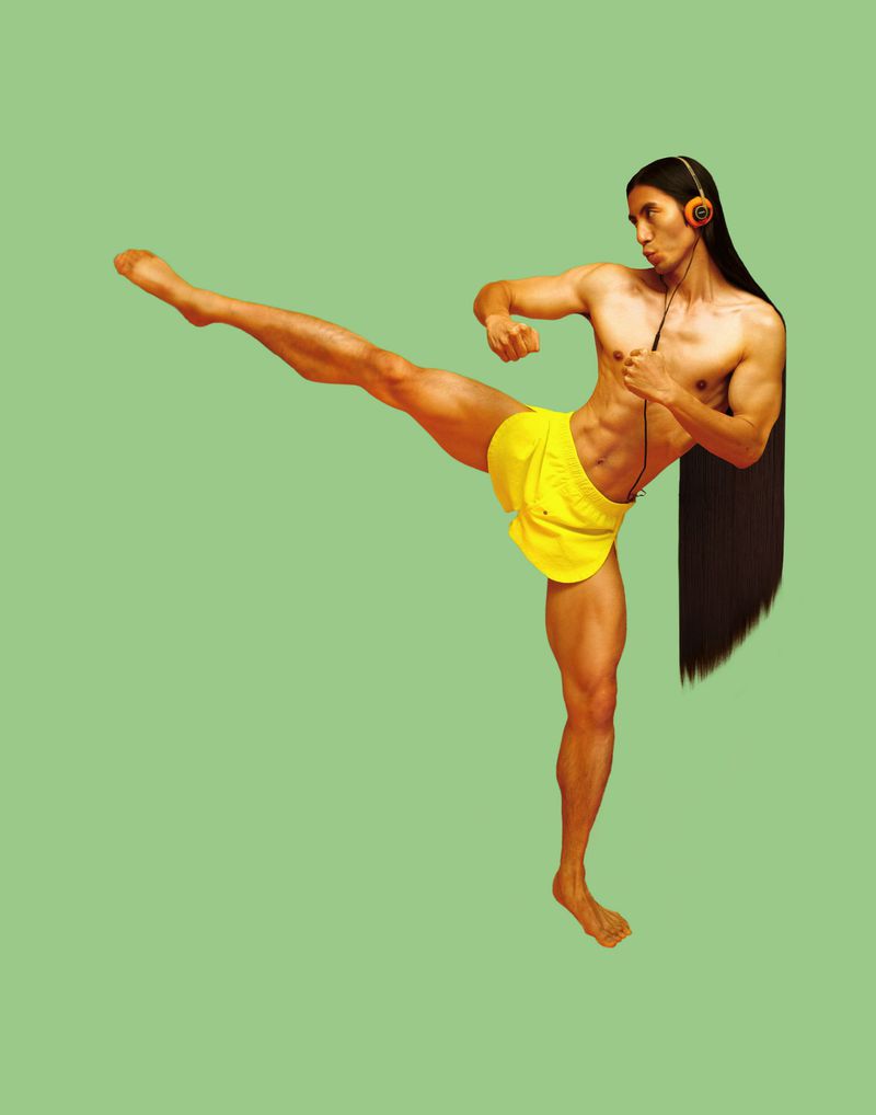 Shirtless man with long hair wearing headphones, yellow shorts, and kicking against a plain green background in a studio shot.