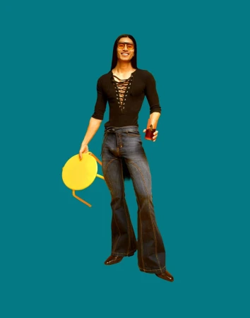 Man in black shirt and bell-bottom jeans stands against teal backdrop, holding a yellow chair and a glass of dark liquid.