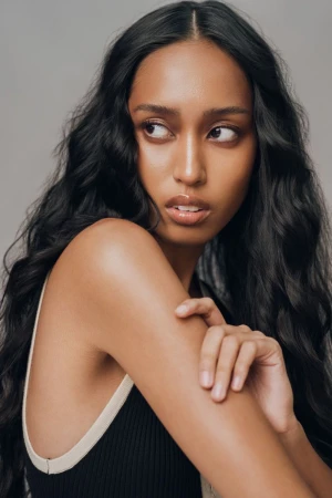 Filipino model with long wavy black hair and dewy makeup looking over her shoulder against a neutral grey studio background.