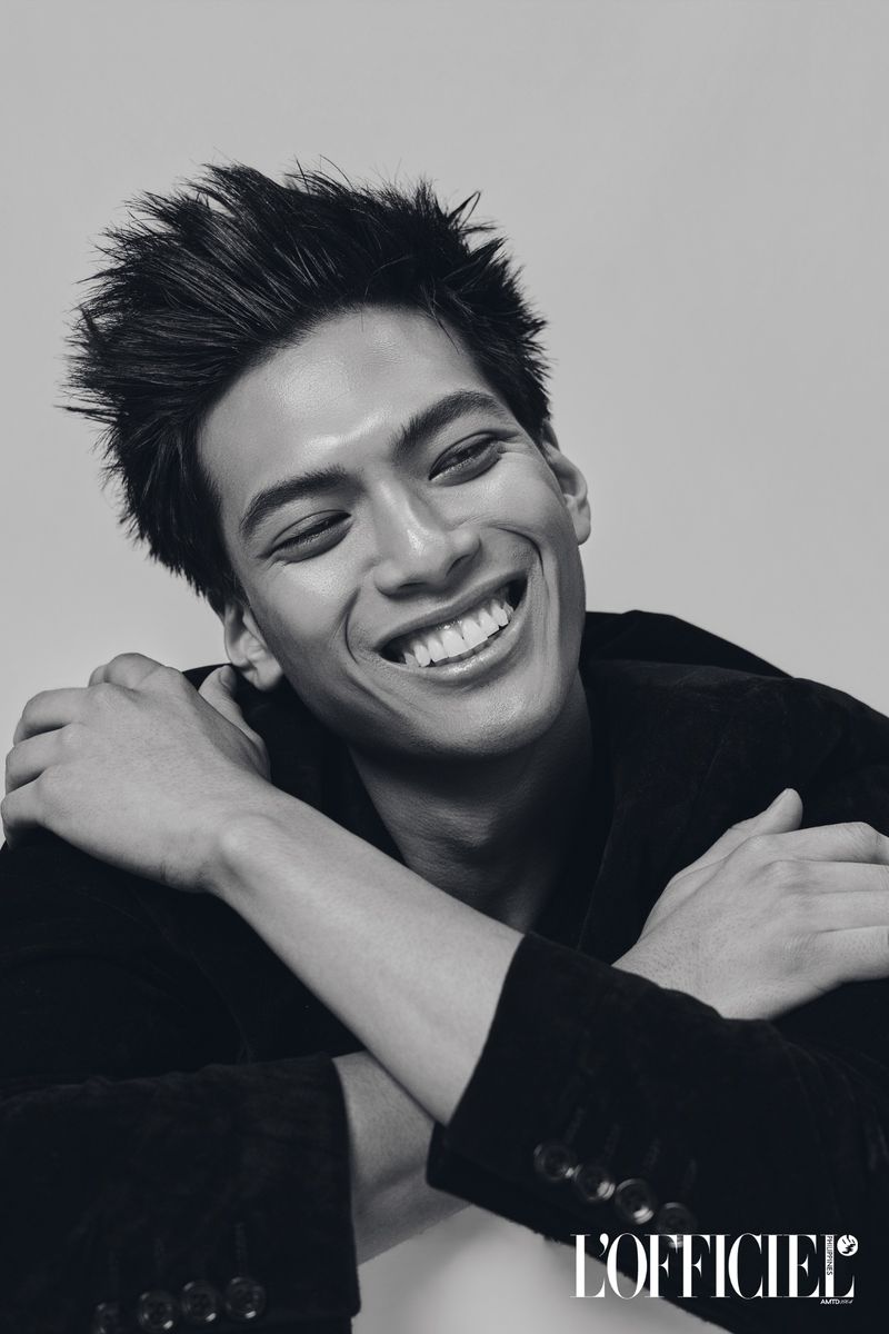 Monochrome portrait of a smiling Filipino man in a dark blazer with arms crossed against a seamless grey backdrop.