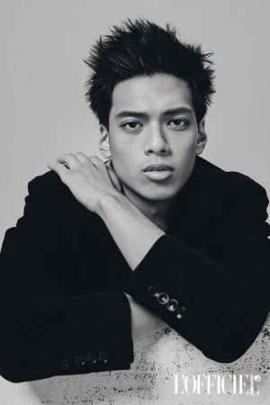Black and white portrait of a young Filipino male model wearing a black blazer and resting his arms on a textured ledge.