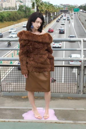 Model Dasha Page in a brown textured fur top and leather skirt standing on an overpass above a busy multi-lane highway.