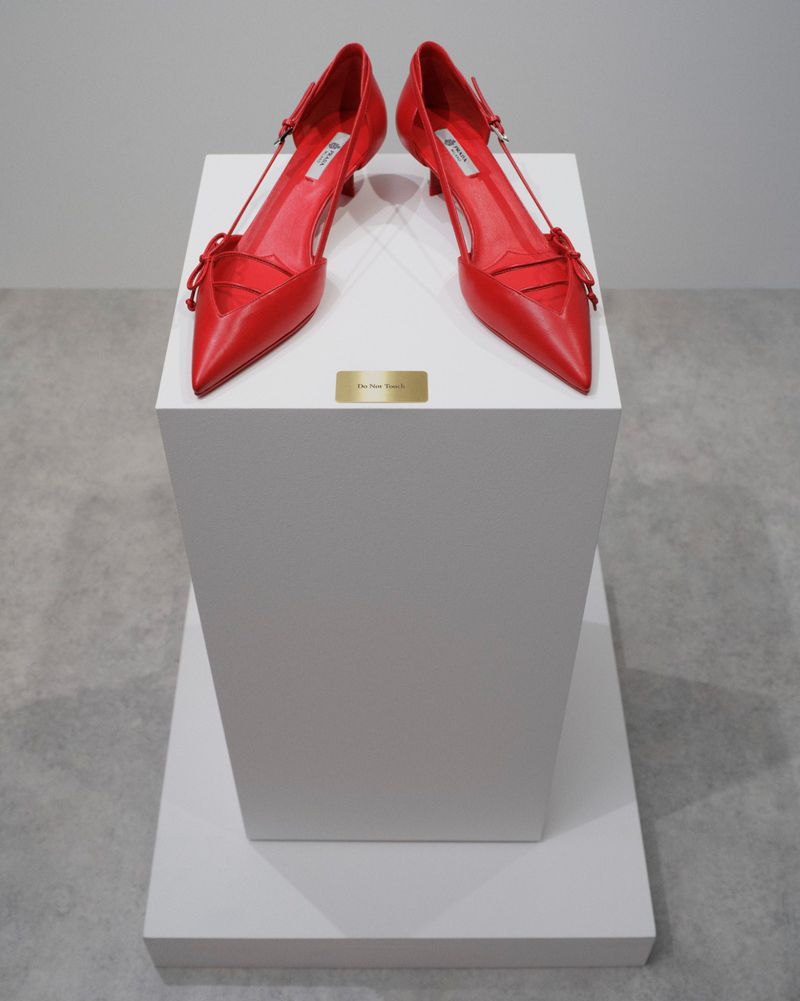 A pair of red pointed-toe slingback heels displayed atop a white gallery pedestal with a small gold plaque.