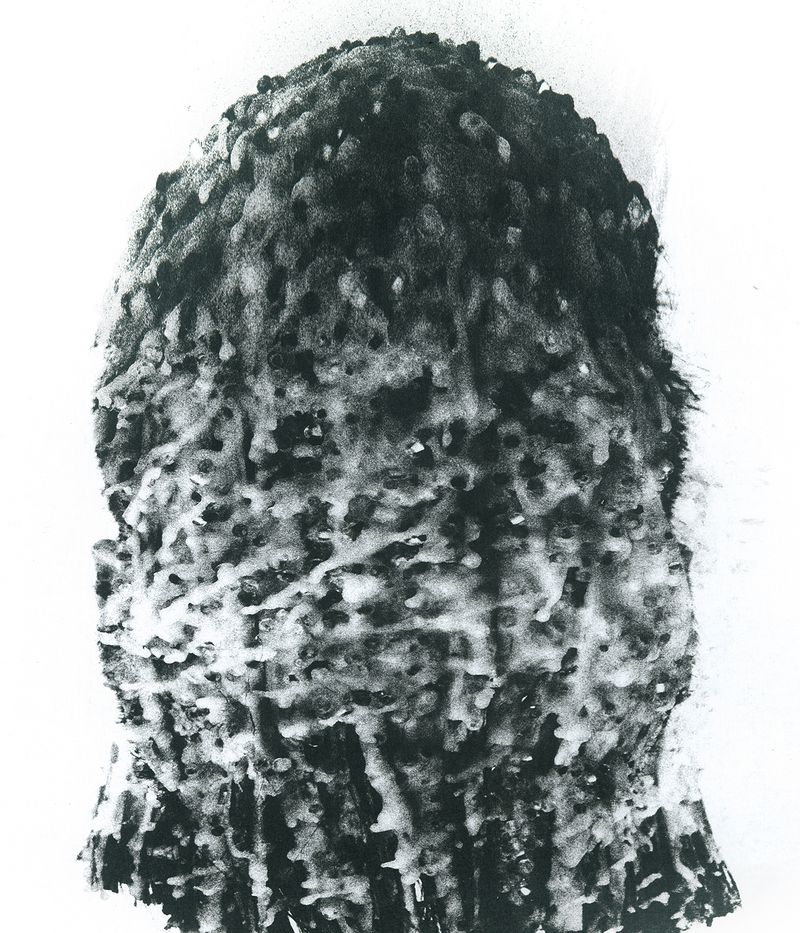 Monochrome close-up of a person's head completely covered in textured, dripping wax against a plain white background.
