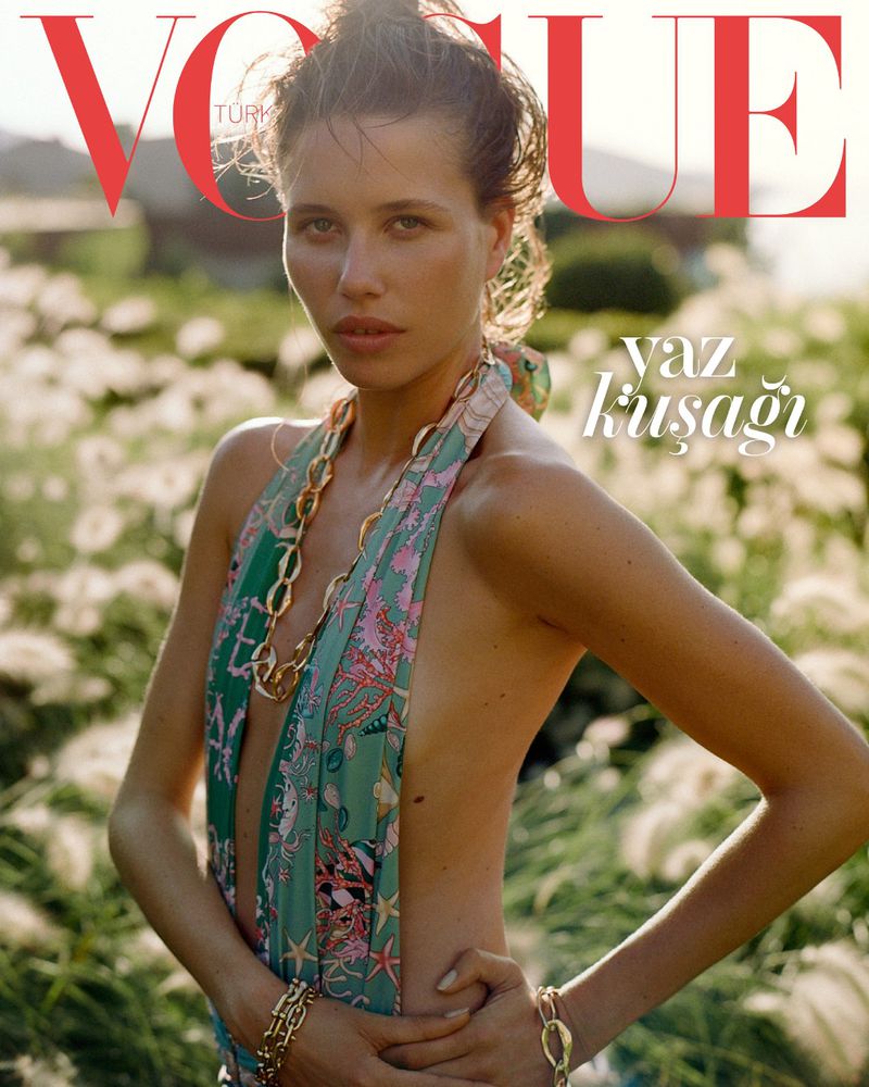 Vogue cover featuring a woman in a patterned swimsuit with gold jewelry, posing in a field of wildflowers, under bright light.