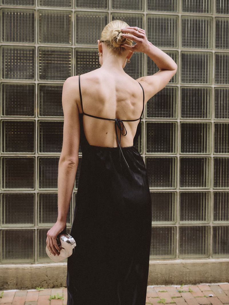 Model in a black slip dress holding a silver clutch against a glass block wall for Abercrombie & Fitch.