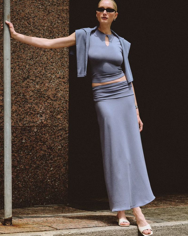 Model wearing a slate blue matching top and maxi skirt set with sunglasses, posing on an outdoor street corner.