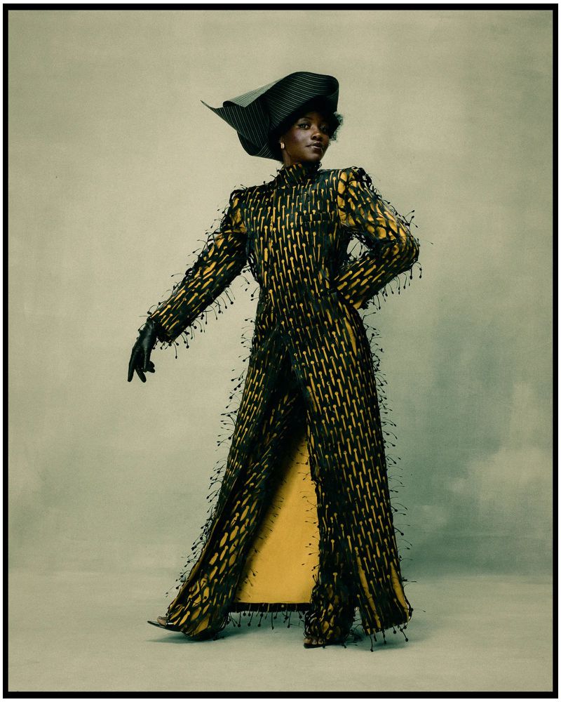 Lupita Nyong'o wearing a sculptural fringed coat and asymmetrical hat in a studio portrait photographed by Kenny Germé.