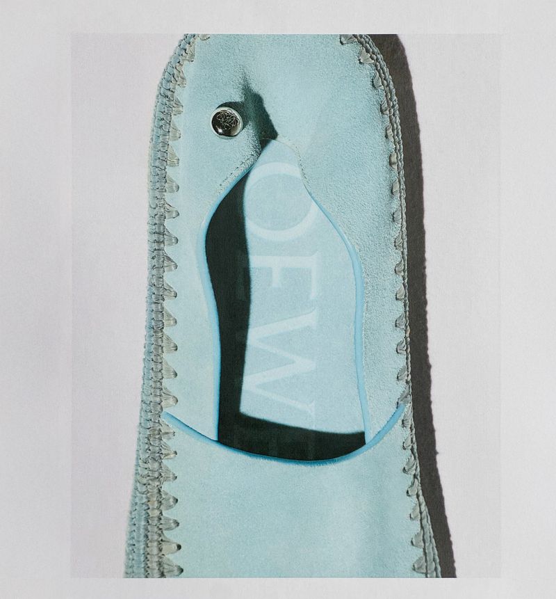 Close-up of a light blue Loewe shoe, showcasing intricate stitching, a metal snap, and the brand's name in a shadowed cutout.