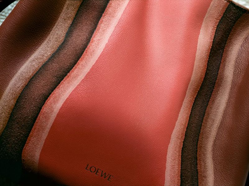 Close-up of a Loewe brand bag showcasing a leather material with brown, tan, and coral wavy stripes creating an abstract pattern.