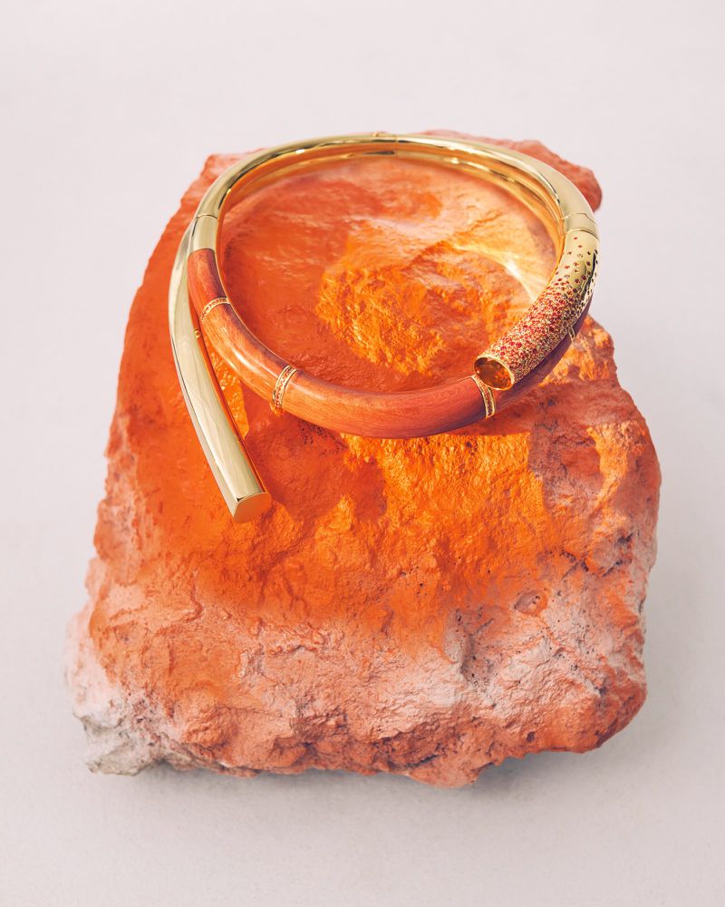 Sculptural gold and coral wrap bracelet resting on a textured orange rock against a pale studio backdrop.