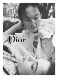 Monochrome close-up of models Zhao Ziqi and Laura Kaiser resting together wearing textured Dior garments with floral brooch.