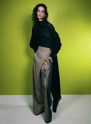 Model in black top and beige patterned wide trousers against a green studio backdrop