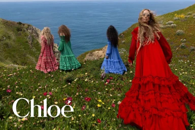 Raquel Zimmermann poses in a red tiered ruffled maxi dress on a wildflower cliff overlooking the ocean with three models.
