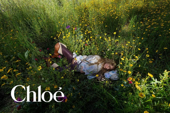 Model in a ruffled bohemian blouse and two-tone leather boots lying down in a field of yellow wildflowers.
