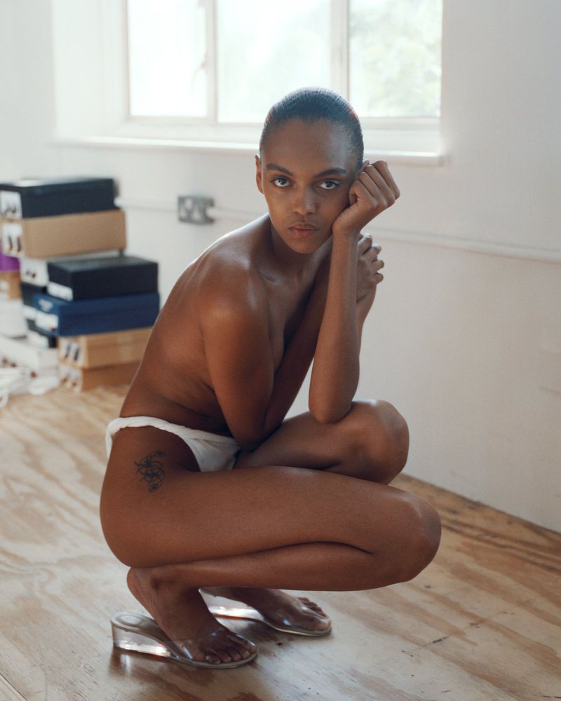 Model crouching on wooden floor wearing white underwear and clear wedge shoes for Supriya Lele