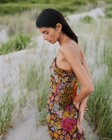 Model Rossana Latallada wearing a colorful floral print slip dress standing among coastal dune grass.