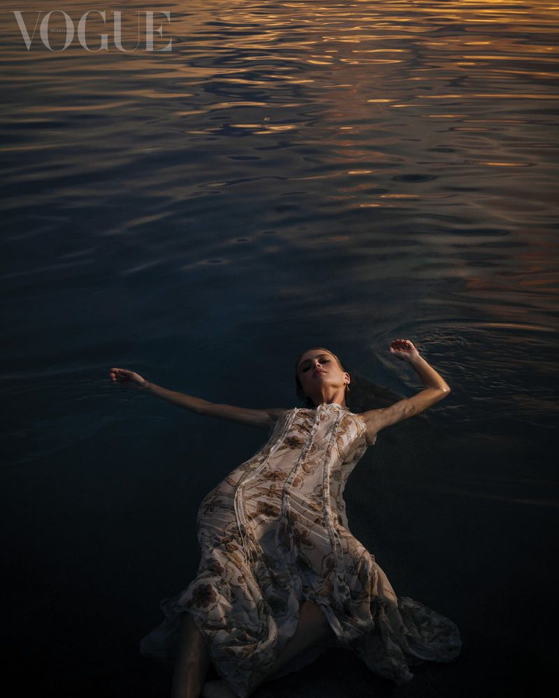 Model floating flat on dark water wearing a patterned dress during sunset for Vogue Latin America