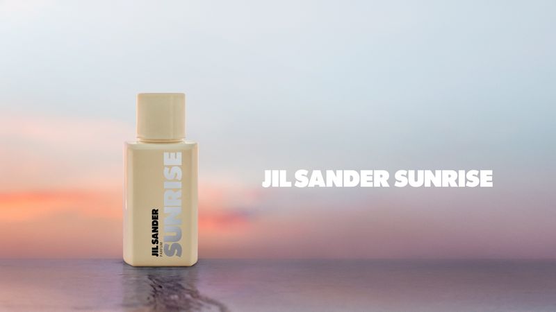 Jil Sander Sunrise perfume bottle on a reflective surface against a blurred sunrise backdrop, showcasing minimalistic beauty product photography.