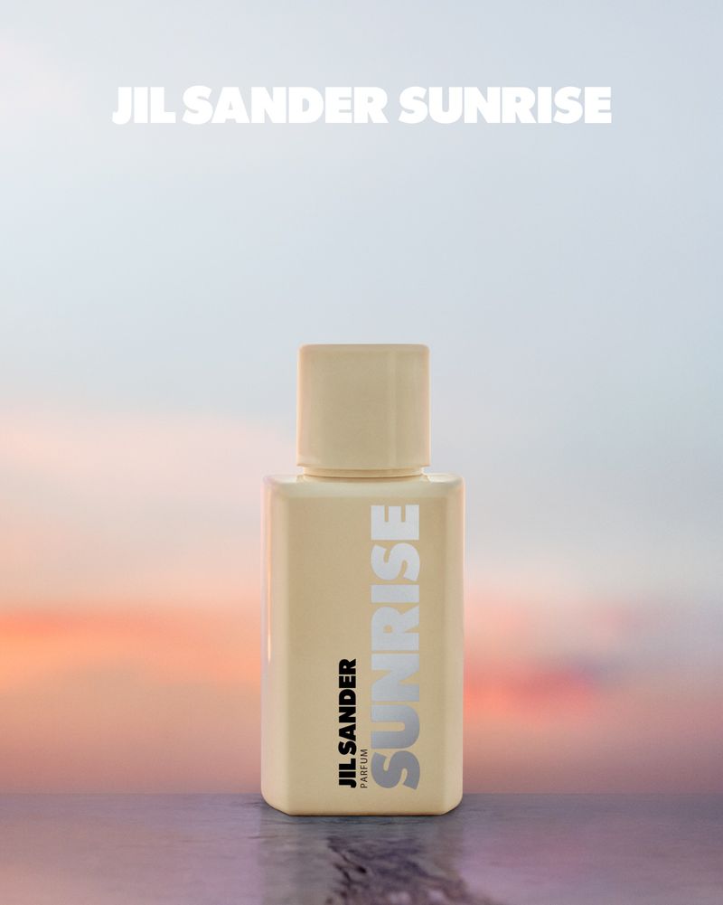 Jil Sander Sunrise perfume bottle on a reflective surface with a blurred sky and sunrise in the background. Beauty product shot.
