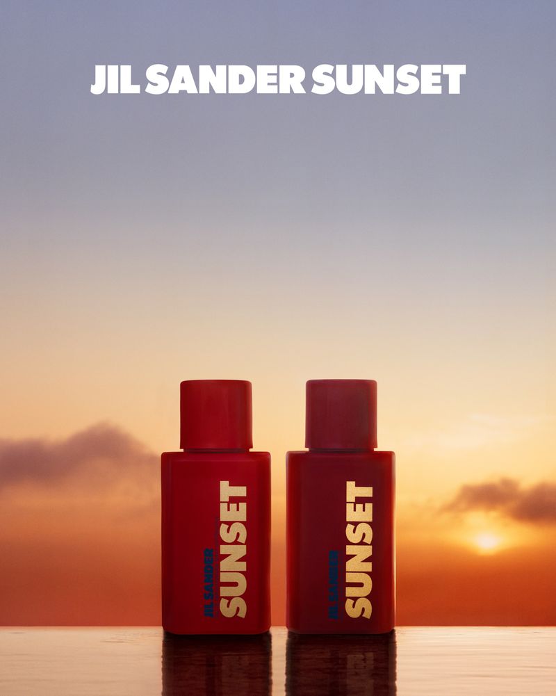 Two JIL SANDER SUNSET perfume bottles stand in front of a sunset sky, product shot, amber, red and gold color palette.