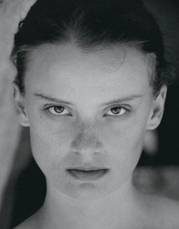 Black and white portrait of a woman with tied back hair and freckles staring directly at the camera in a close-up headshot.