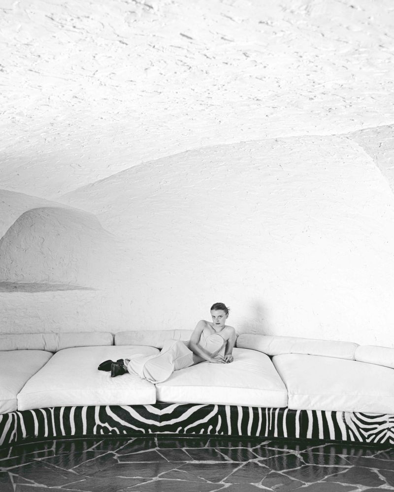 Adult female model lounges on a large modular sofa with a zebra-print base, set against a white backdrop in a photo studio.