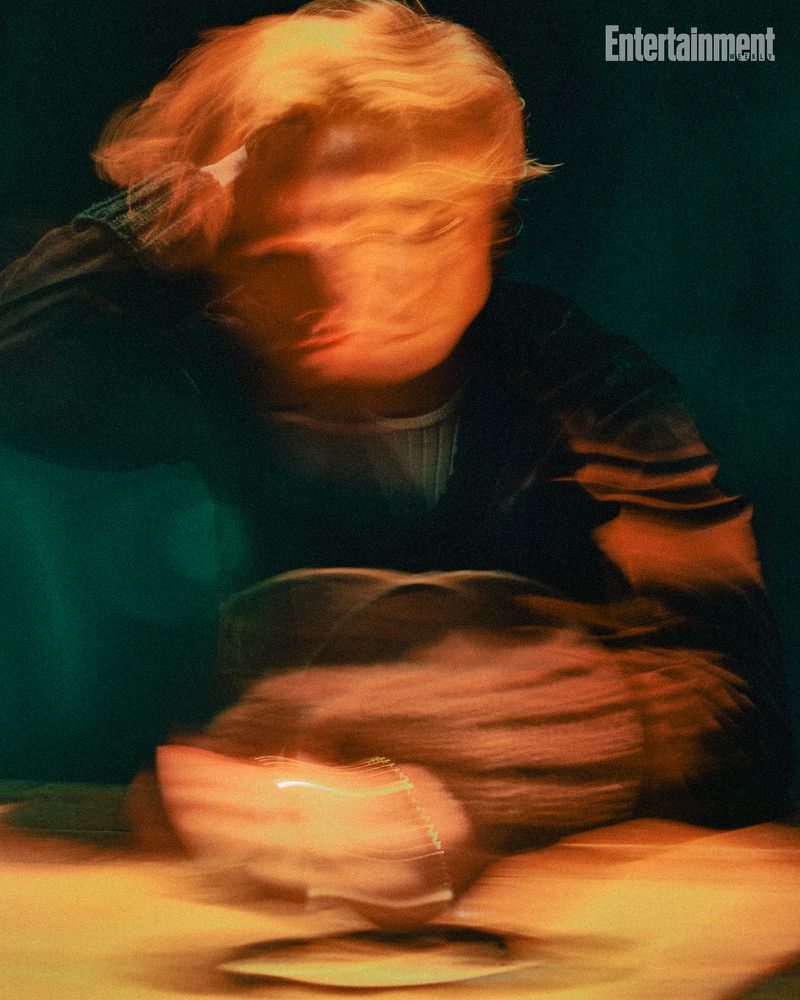 Motion blurred editorial portrait of Tom Rhys Harries leaning over a wooden table under warm amber lighting.