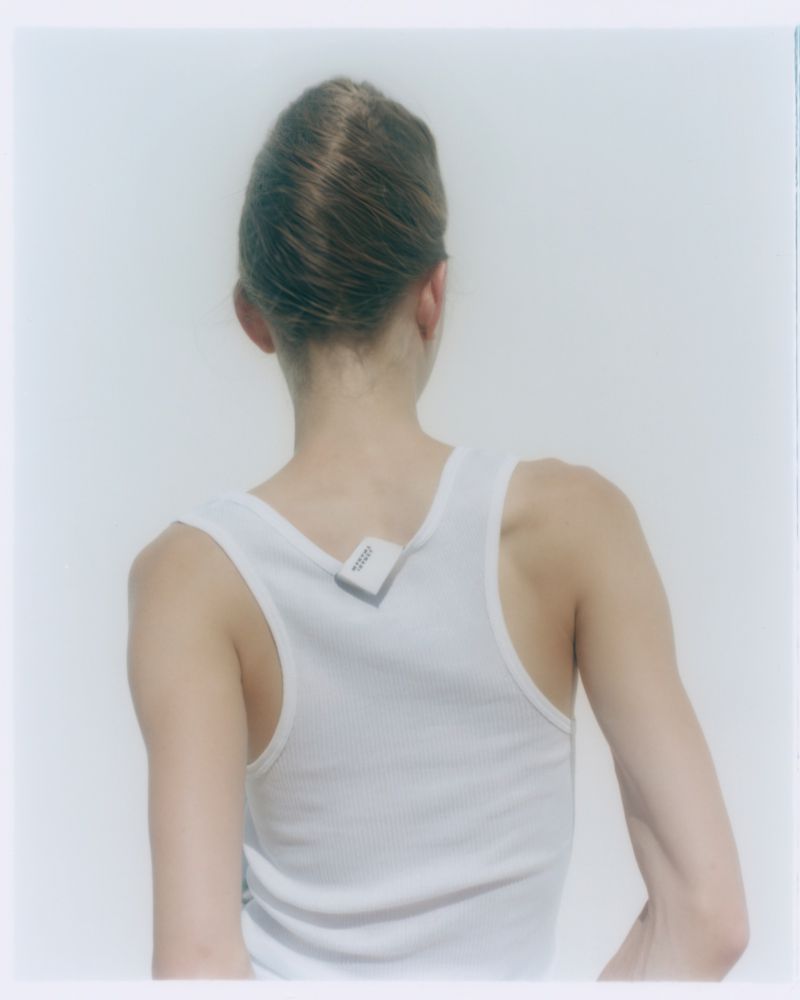 Back view of a young adult female with updo wearing a white tank top; a small sensor device is attached to the upper back.